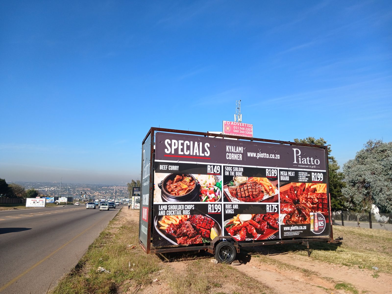 Piatto restaurant specials board on a Simply Visible trailer beside a busy highway at Kyalami Corner